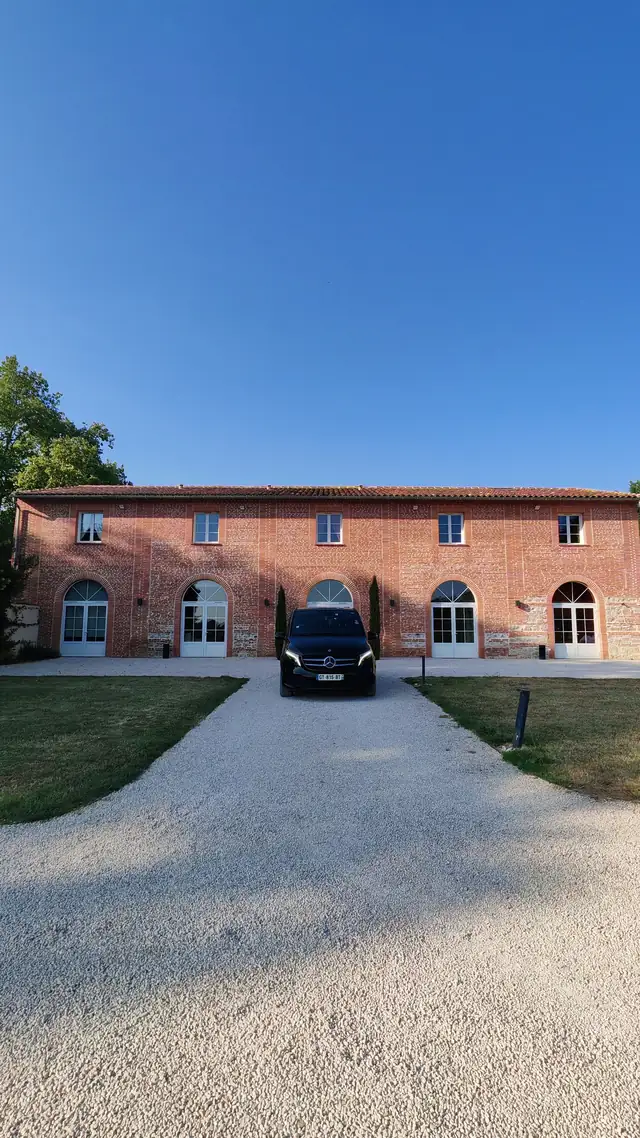 Van Mercedes Classe V avec chauffeur devant l'allée d'un domaine de mariage en brique toulousaine